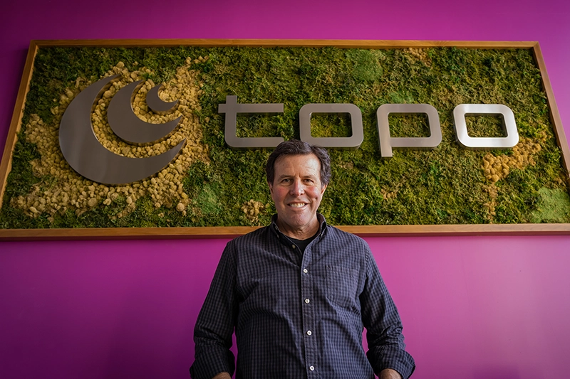 Tony Post with Topo logo behind him at corporate office.