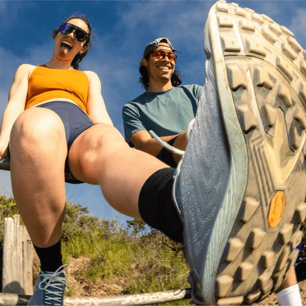 Low angle shot of two runners sitting on fence showing bottom of Topo trail shoe